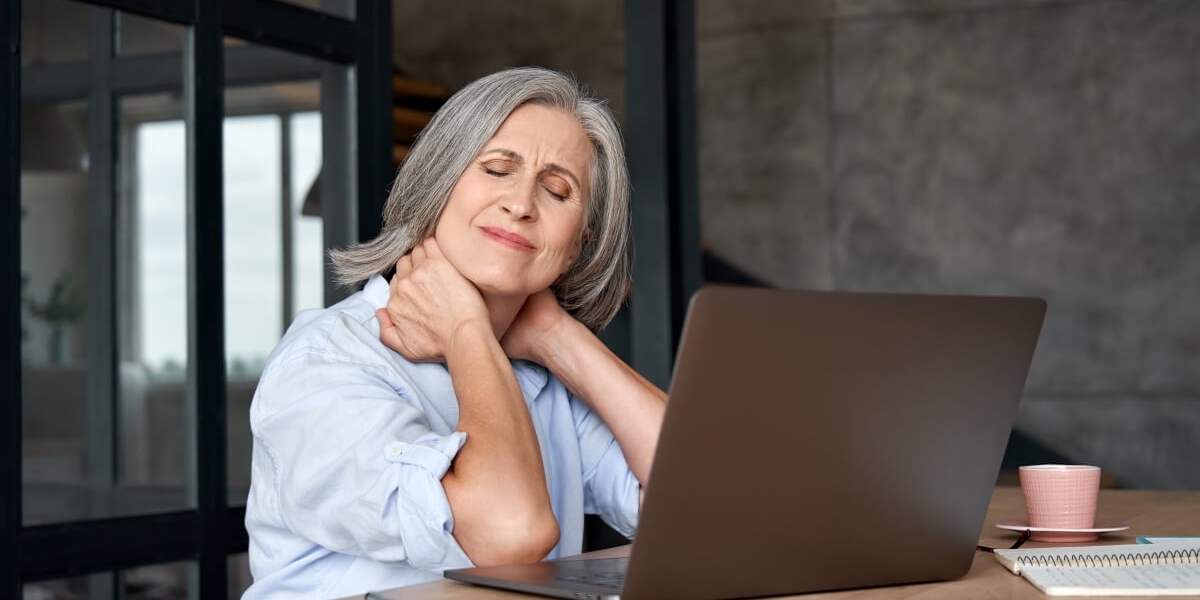Donna in menopausa davanti al laptop manifesta dolori articolari all'altezza del collo